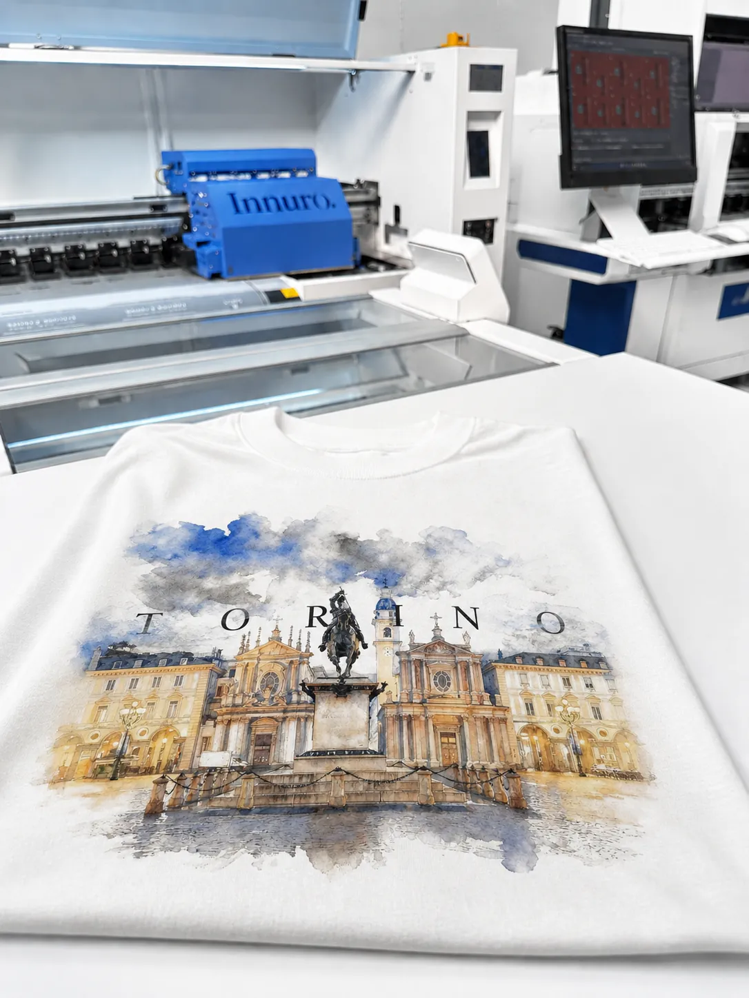 Camiseta blanca con ilustración acuarela de Torino impresa con DTI junto a una impresora Innuro